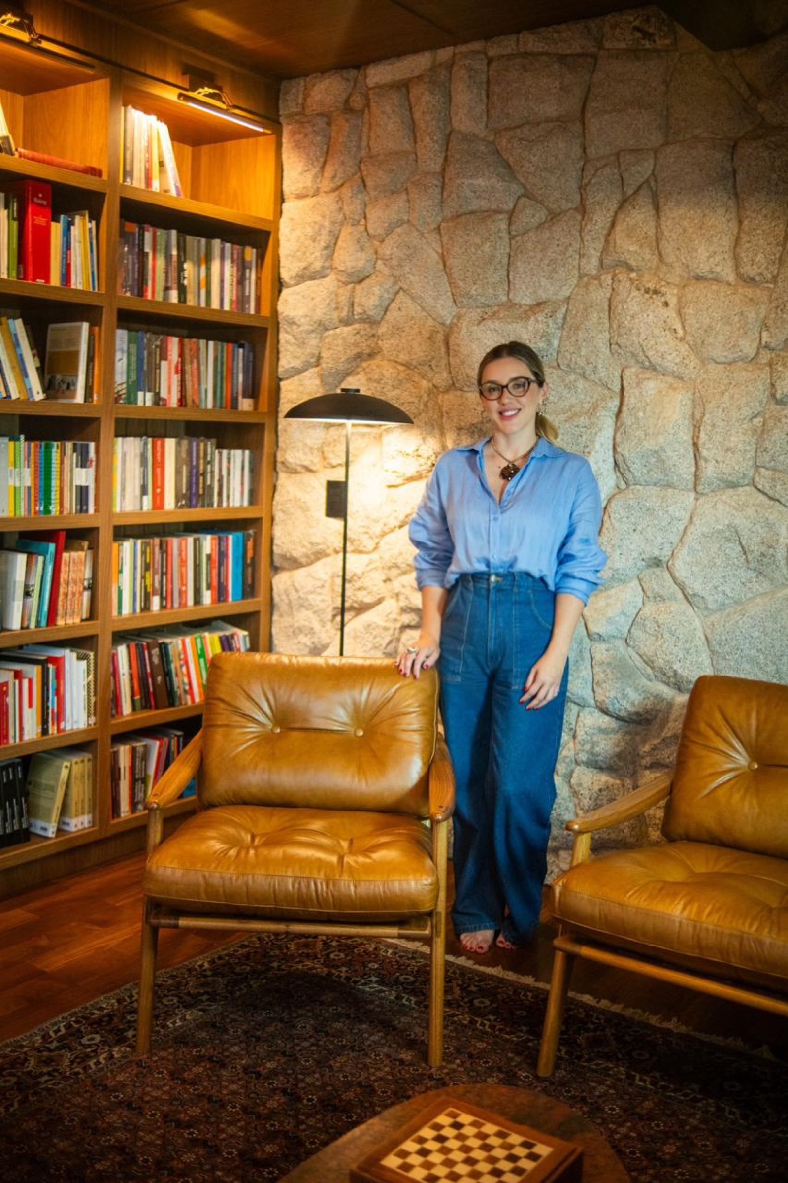 Lily Zemuner em sala com poltronas de couro e parede de pedra
